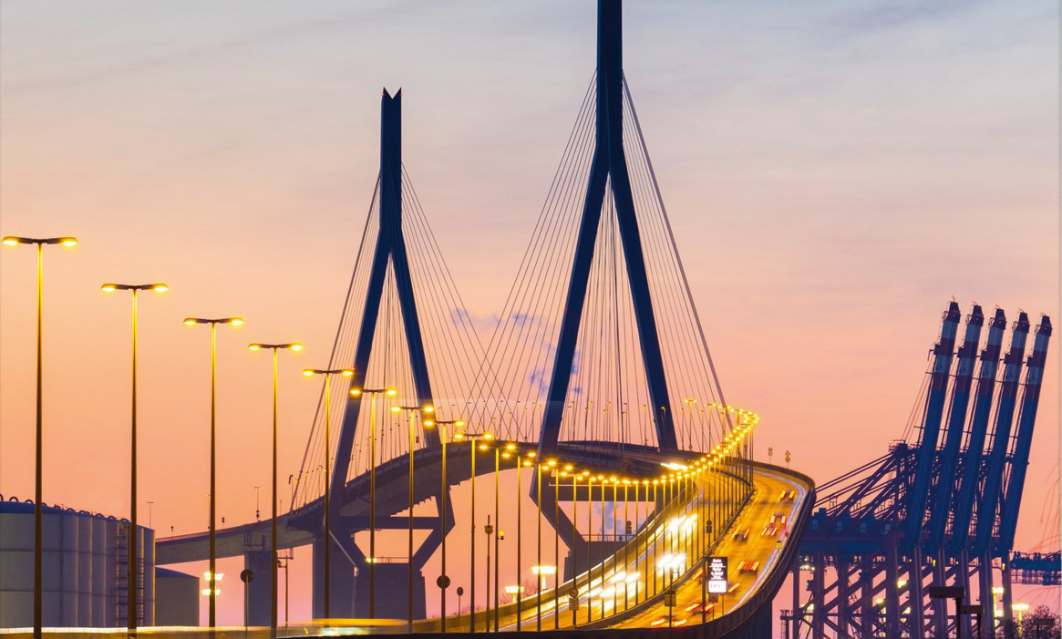 Die Köhlbrandbrücke in der Abenddämmerung mit Hamburger Hafenkränen im Hintergrund