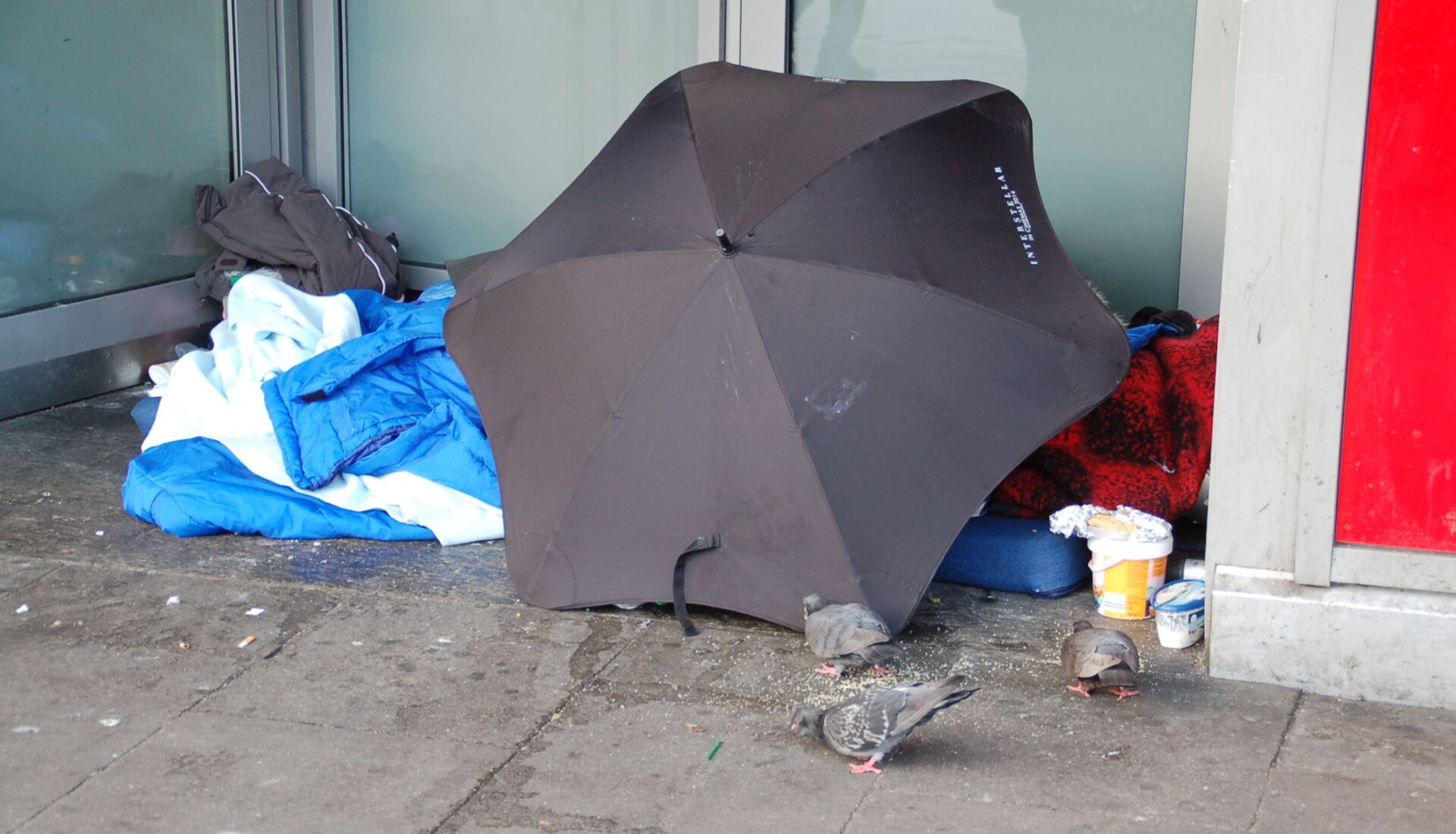 Schlafplatz eines Obdachlosen nur geschützt durch einen aufgespannten Regenschirm