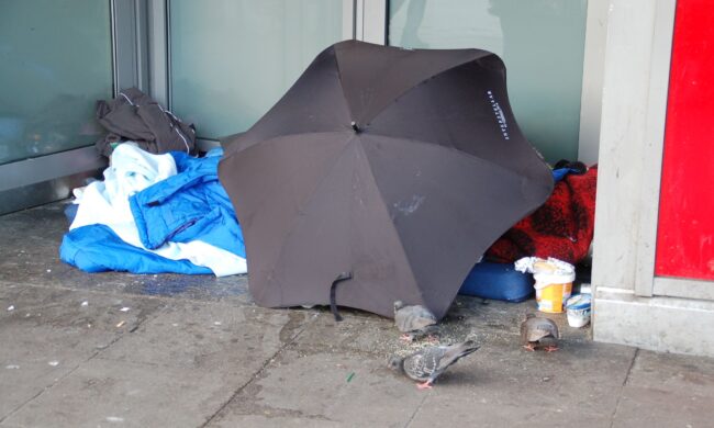 Schlafplatz eines Obdachlosen nur geschützt durch einen aufgespannten Regenschirm