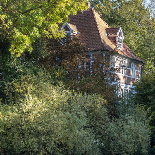 Ein altes Fachwerkhaus umgeben von Bäumen und Pflanzen, nahe am Wasser