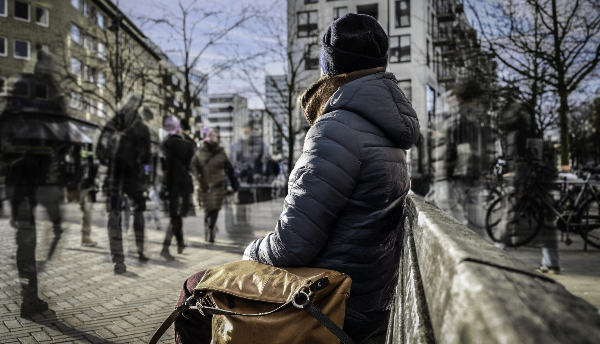 Eine Frau sitz alleine auf einer Bank in einer belebten Innenstadt