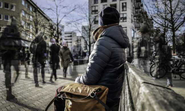 Eine Frau sitz alleine auf einer Bank in einer belebten Innenstadt